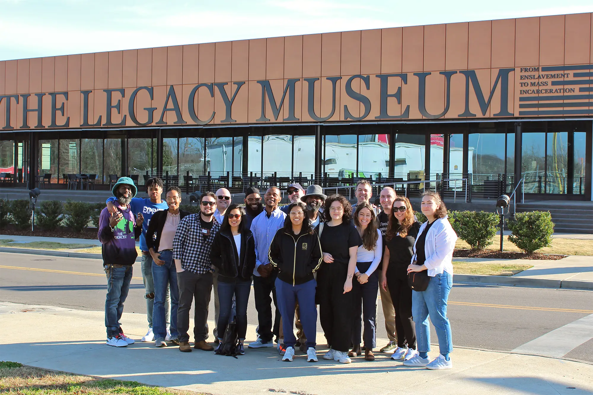 The Freedom Reads team all gathered together in front of The Legacy Museum in Montgomery, Alabama. The museum signage has a smaller subtitle to the right, reading “From Enslavement to Mass Incarceration.”