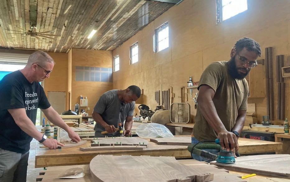 Three members of the Freedom Reads team work inside the Revival Workshop on wooden bookcases at various stages of completion.