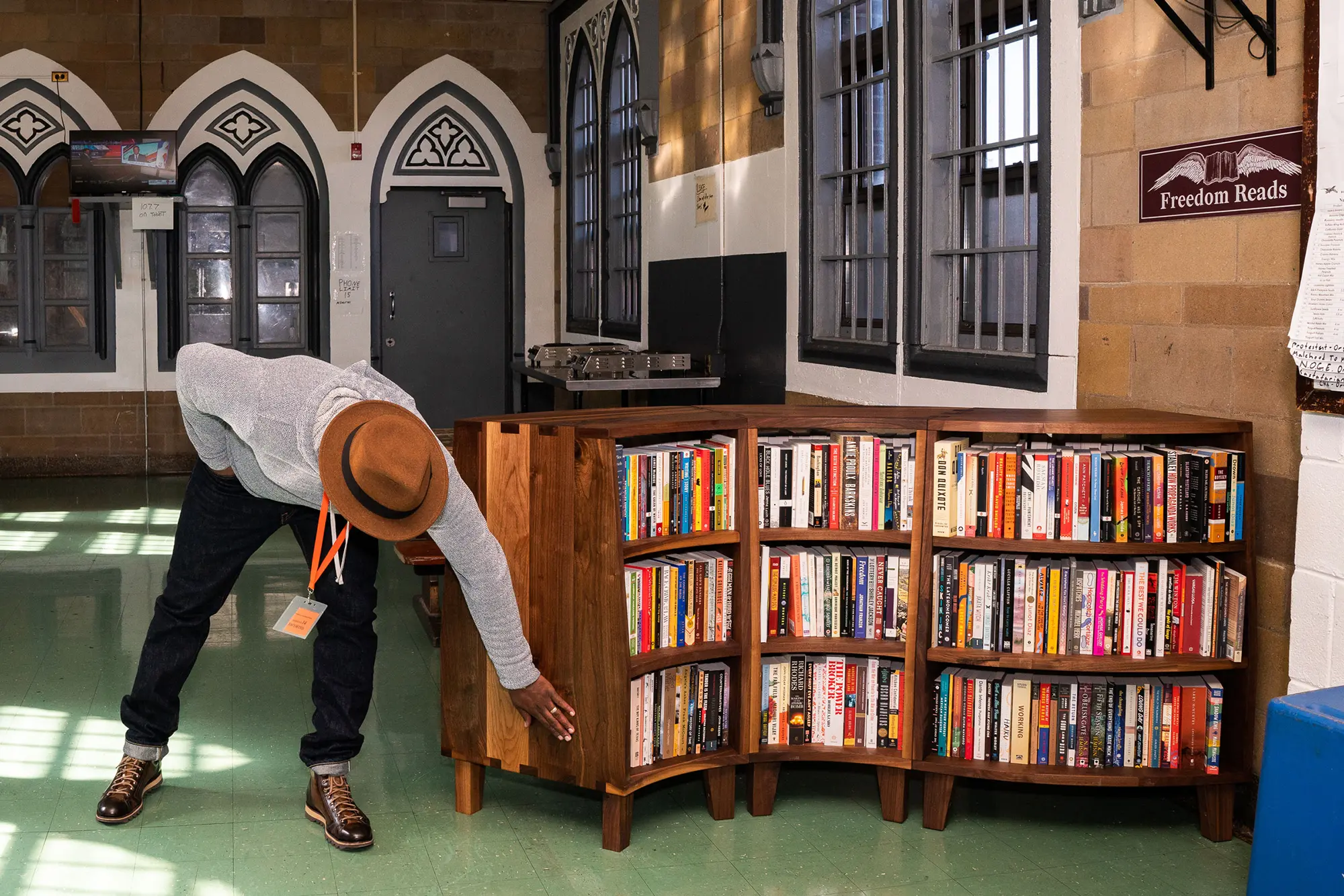 Reginald Dwayne Betts leans down, passing his hand over the smooth wooden side of a curved Freedom Library filled with books at Woodbourne Correctional Facility in New York.