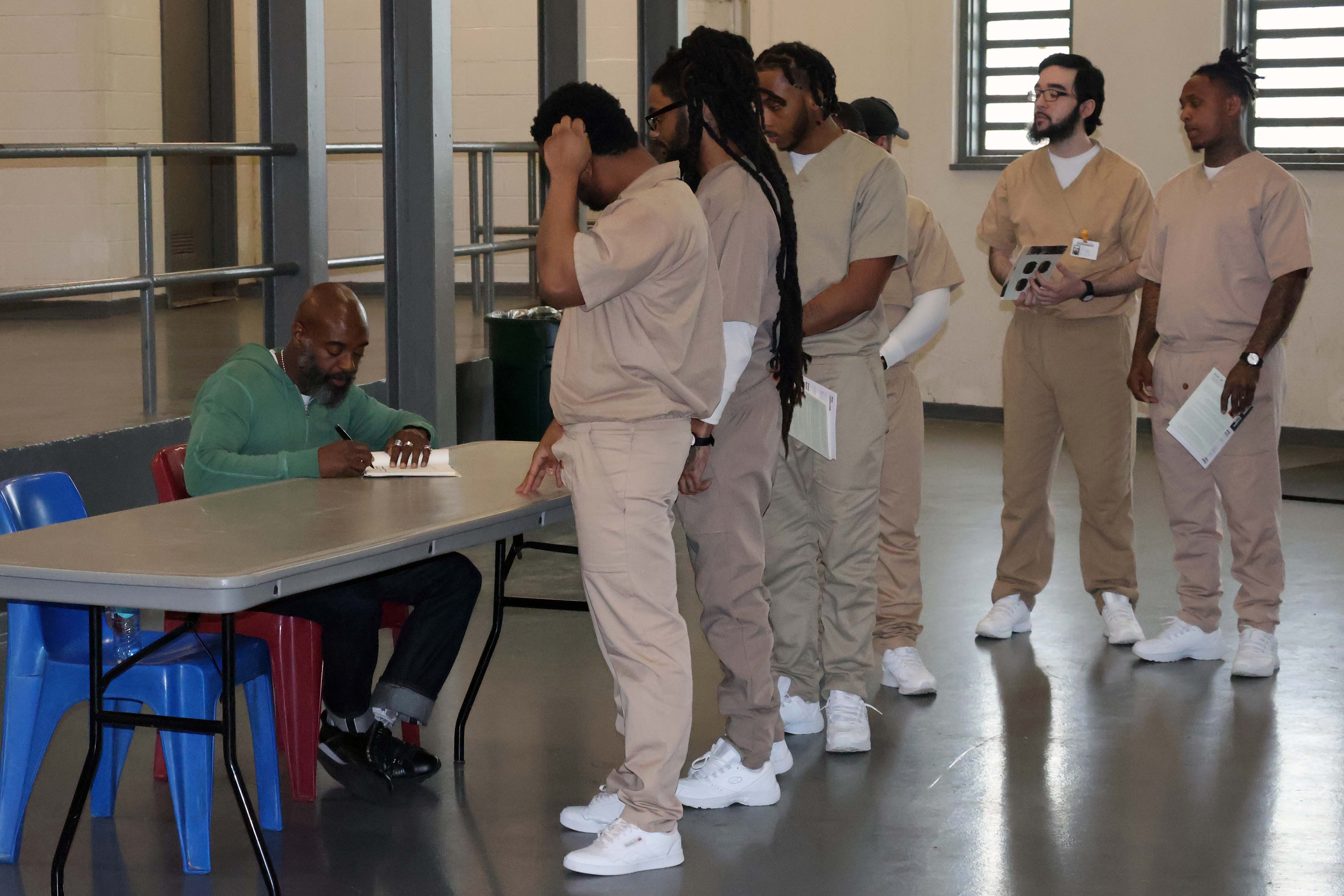 6 men at Garden State Correctional Facility line up to have copies of FELON signed by Freedom Reads Founder & CEO Reginald Dwayne Betts, who sits at a table.