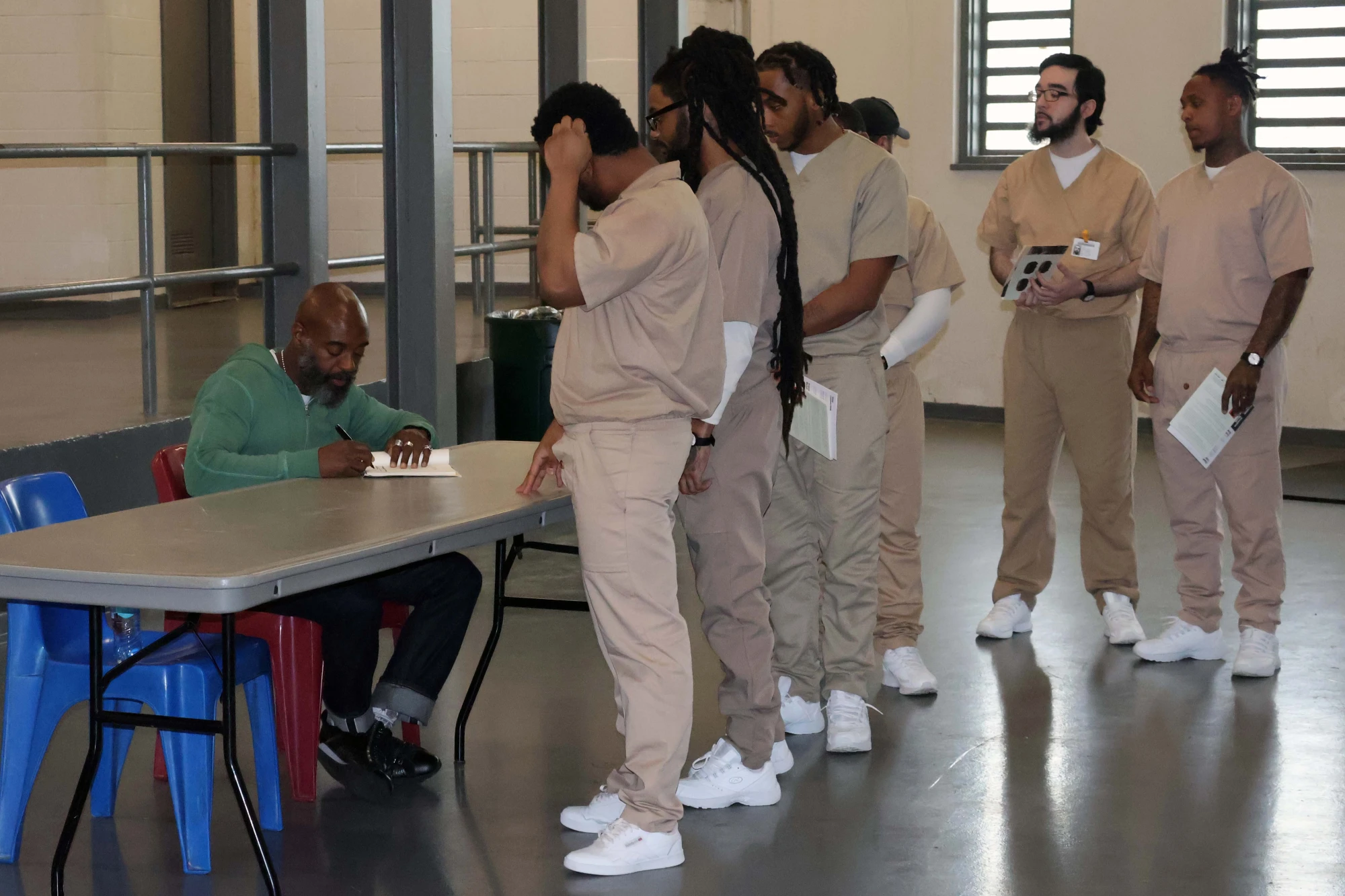 6 men at Garden State Correctional Facility line up to have copies of FELON signed by Freedom Reads Founder & CEO Reginald Dwayne Betts, who sits at a table.