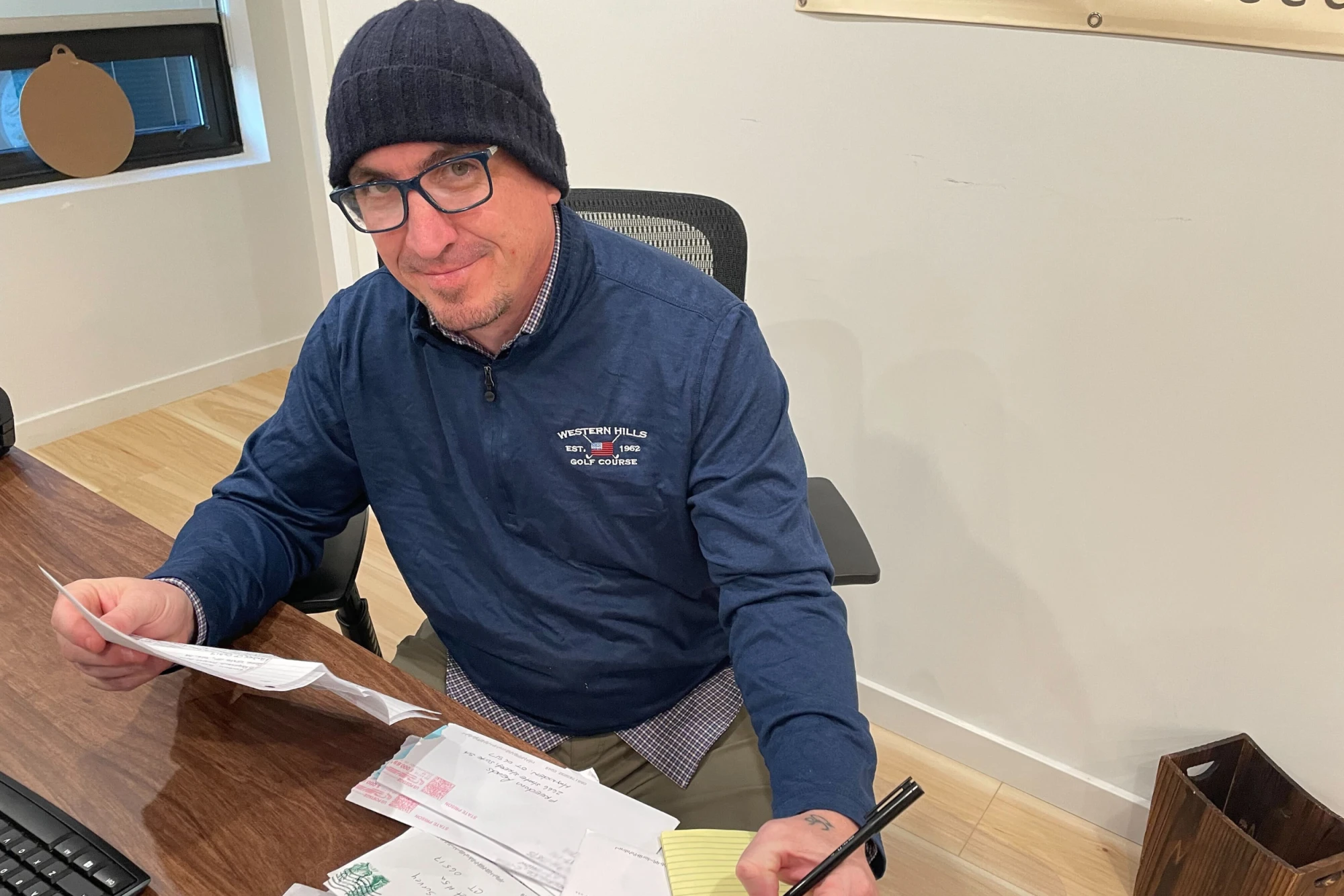 Freedom Reads Communications Manager Steven Parkhurst sits at a desk with letters in hand, smiling at the camera.