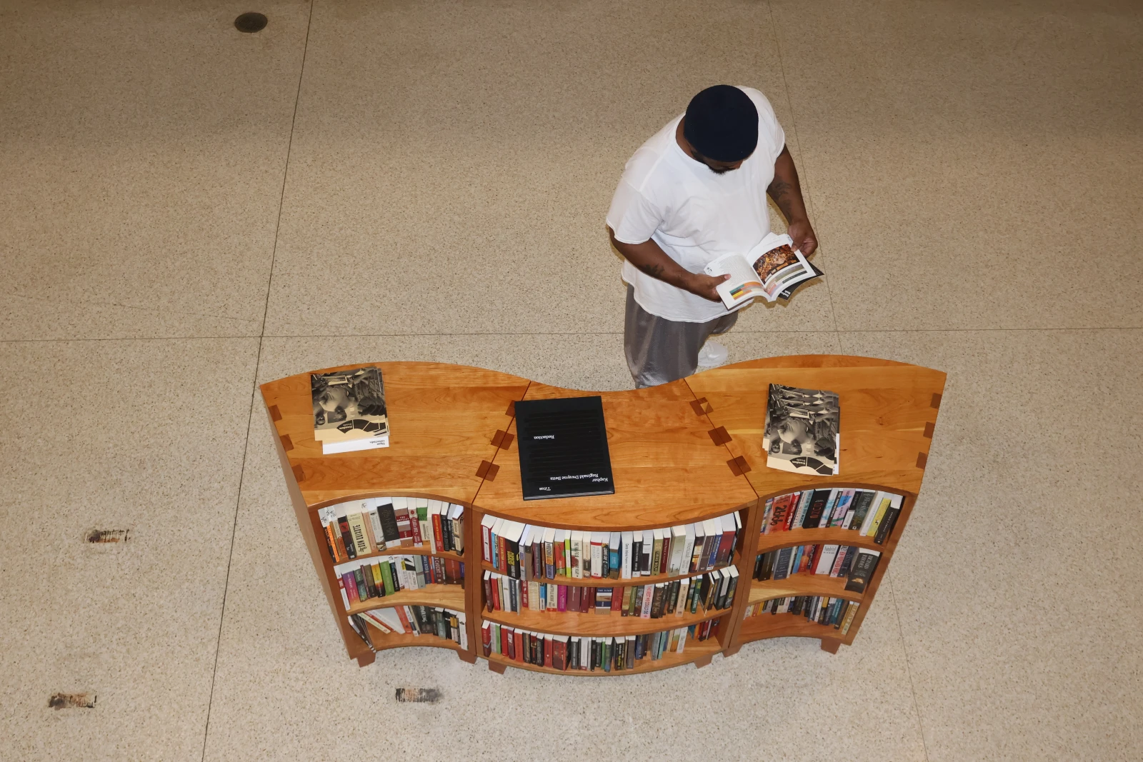 Freedom library curved bookcase from above with a library patron wearing a white t-shirt and gray shorts reading a book.