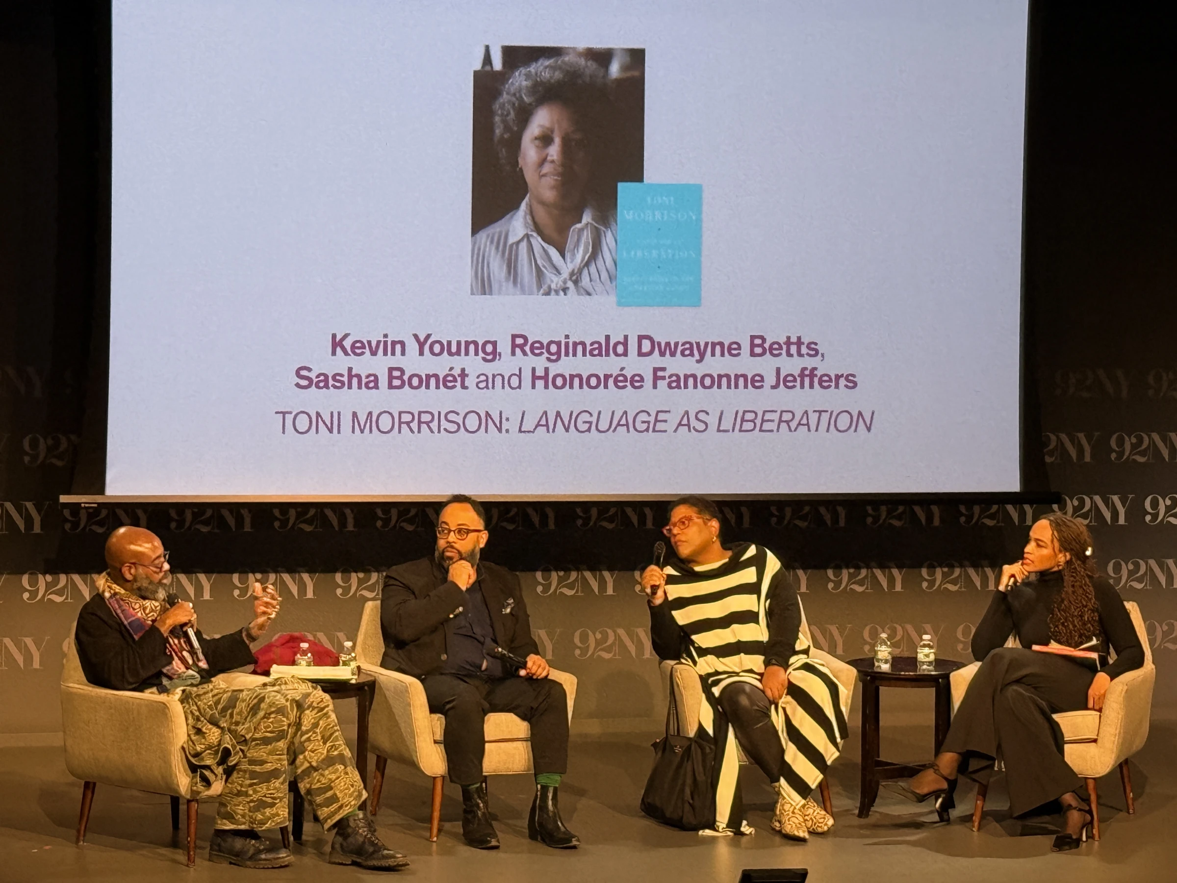 4 speakers on stage with presentation screen behind them