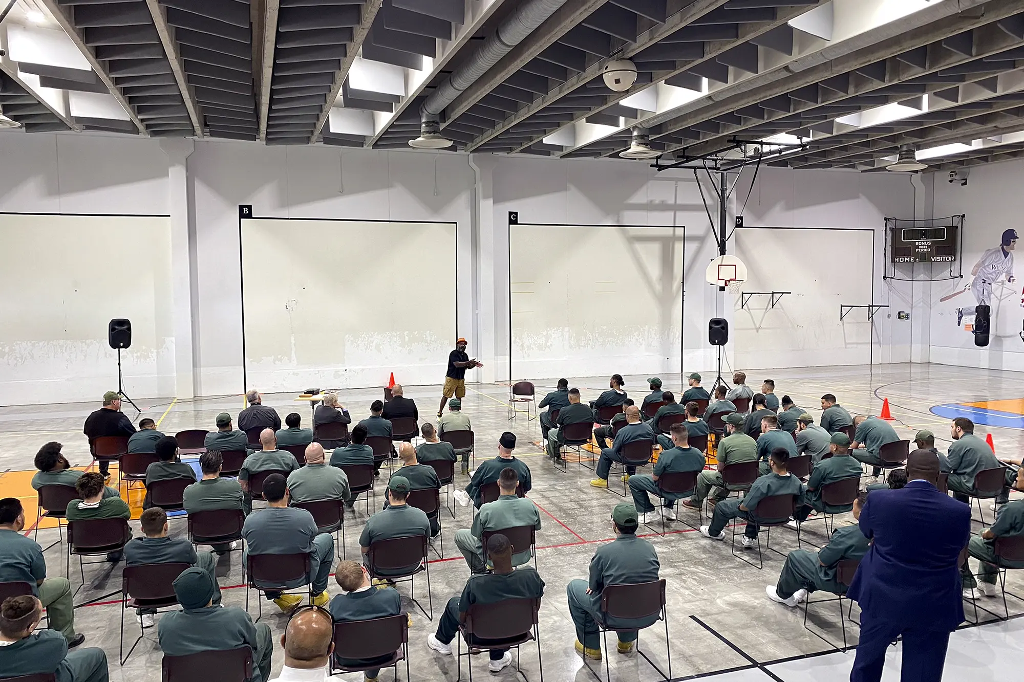 Reginald Dwayne Betts performs in a large gymnasium filled with seated men at Arkansas Valley Correctional Facility in Colorado.